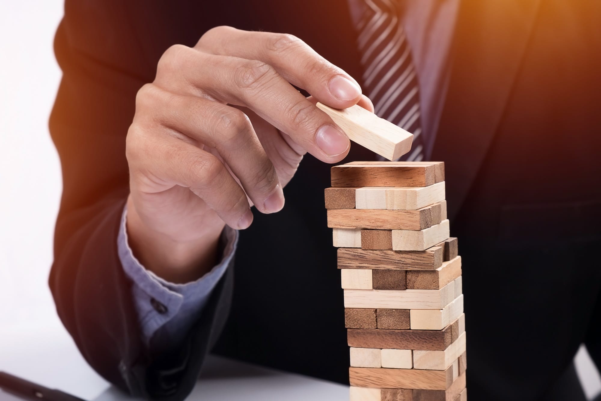 A person in a suit carefully removes a wooden block from a stacked tower game, resembling Jenga, demonstrating the focus and strategy required to master a garden center CRM.