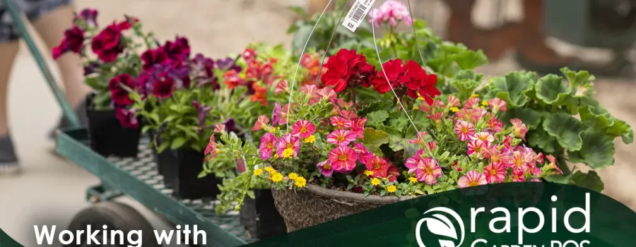 A garden center worker pulls a cart filled with colorful potted flowers and plants. Text: "Working with Promotions in Counterpoint" -- A Rapid Garden POS webinar.