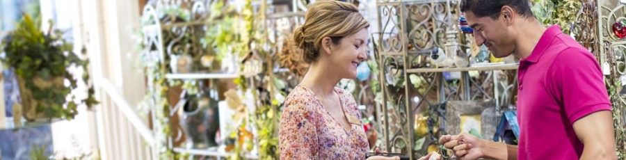 Woman checking price of a small item for a customer in a garden center.