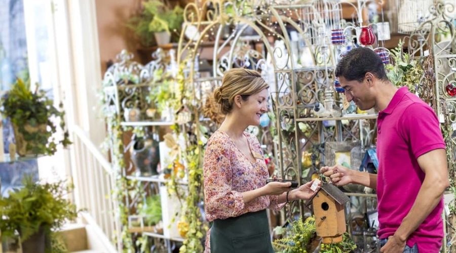 Woman checking price of a small item for a customer in a garden center.